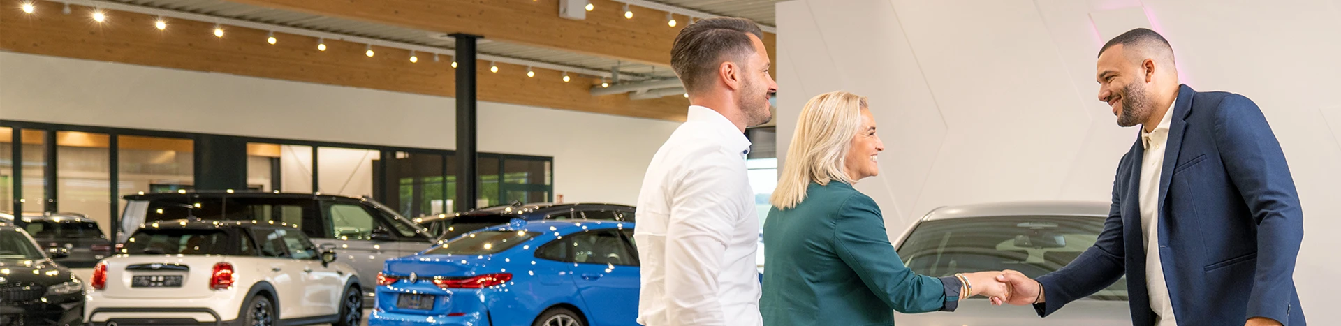 Ein Verkaufsberater begrüßt seine Kunden zur Fahrzeugübergabe ihres neuen und preiswerten Gebrauchtwagens.