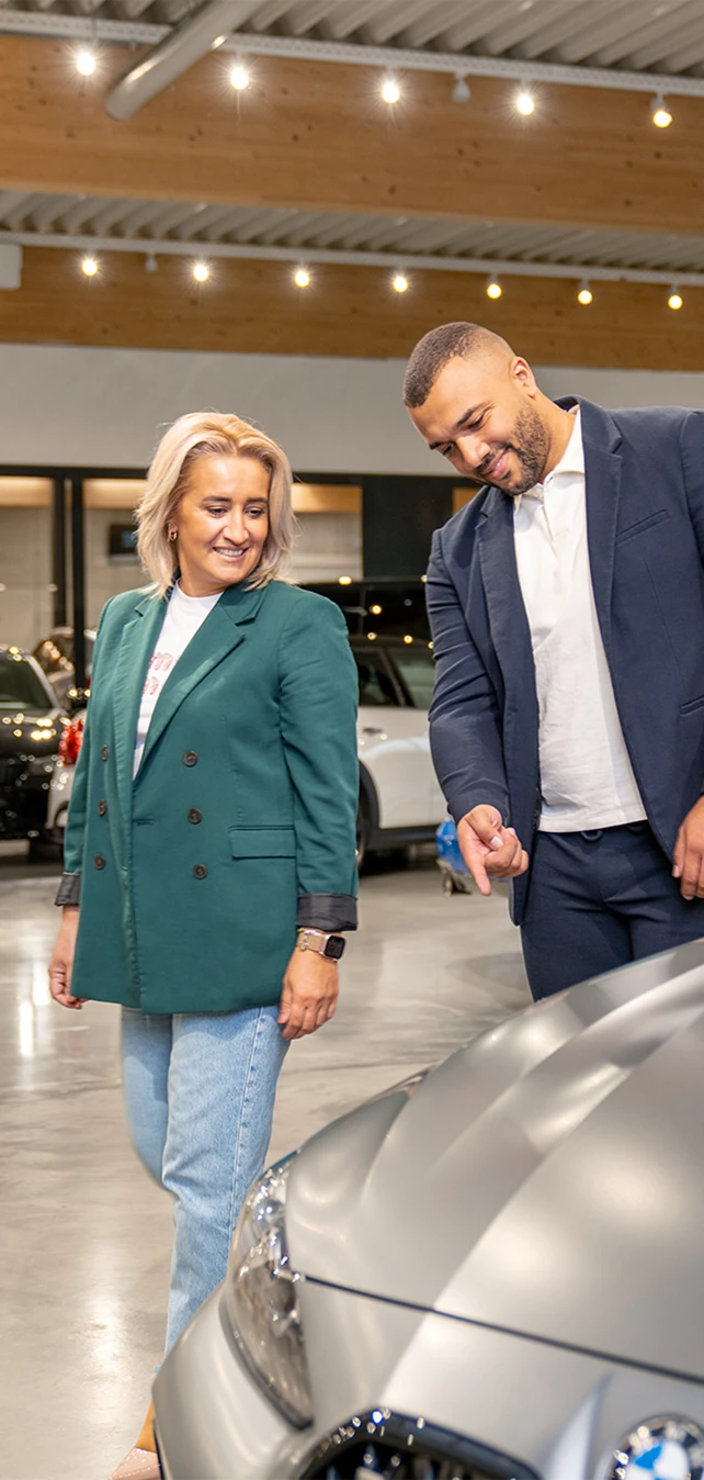 Ein Verkaufsberater zeigt einer Kundin ihr neu erworbenes Gebrauchtfahrzeug.