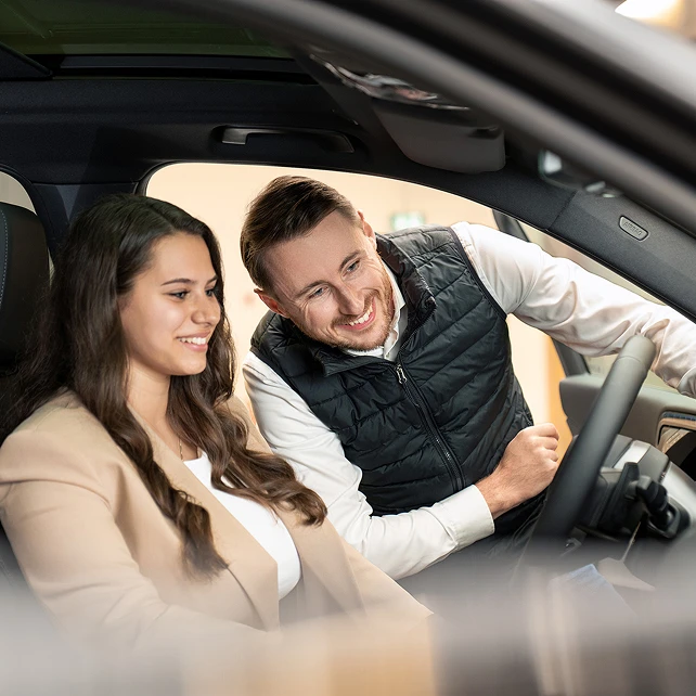 Einer Kunden wird ihr neu erworbenes und preiswertes Fahrzeug von einem Verkaufsberater erklärt.